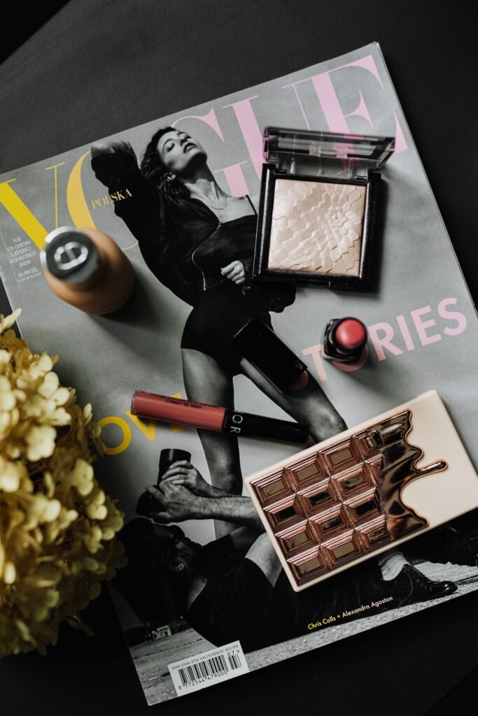 Elegant makeup flat lay with highlighter, lipstick, lip stain, foundation, and makeup palette on a fashion magazine