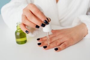 Woman applying cuticle oil to glossy black manicured nails as part of a nail-care routine.