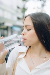 Woman drinking water from a clear bottle to stay hydrated and support healthy, glowing skin.