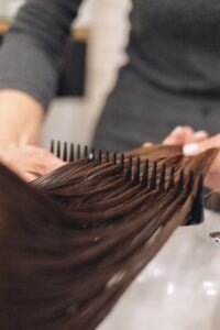 Hairstylist combing damp brown hair with a wide tooth comb for detangling by Aymax Blush