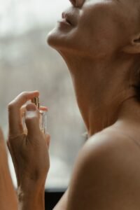 Woman applying perfume to her neck with a glass fragrance bottle | Aymaxblush