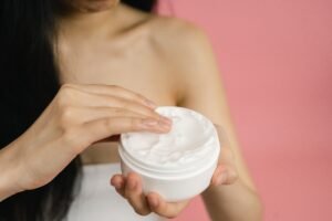 Woman holding an open jar of white facial moisturizer cream for a daily skincare routine.