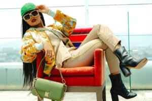 Stylish woman wearing a colorful floral jacket, beige outfit, green cap, sunglasses, and black boots for a trendy fashion look