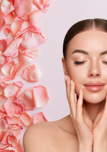 Woman touching her face with soft pink rose petals beside her, representing a gentle skincare routine and healthy glowing skin