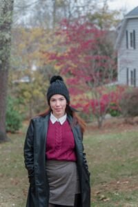 Woman wearing a burgundy sweater, black leather coat, plaid skirt, and beanie for a stylish fall outfit