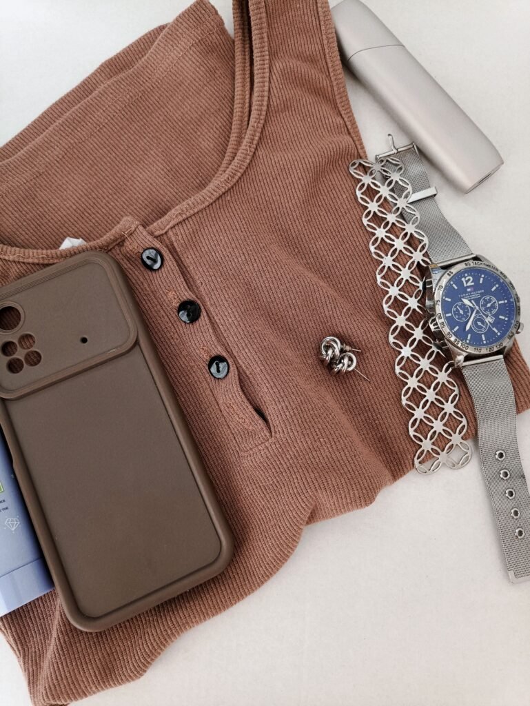 Women’s fashion accessories with brown knit top, silver watch, bracelet, earrings, and smartphone