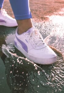 White Puma sneakers stepping through shallow water in sunlight