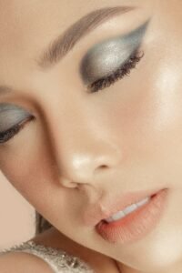 Close-up glam makeup look with metallic silver eyeshadow, defined lashes, glowing skin, and peachy nude lips
