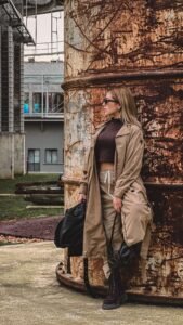 Trendy 2026 modern outfit with beige trench coat, brown crop top, relaxed pants, boots, and black handbag