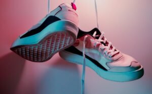 White and black sporty sneakers with laces displayed under pink and blue lighting
