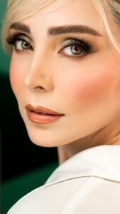 Close-up beauty makeup look with glowing skin, soft brown eyeshadow, defined lashes, peach blush, and glossy nude lips