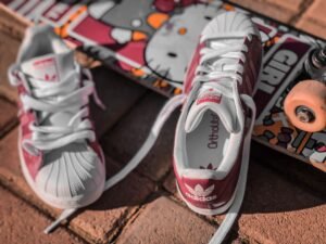 White and pink Adidas sneakers with a skateboard on a brick surface
