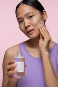 Woman applying toner to her face while holding a toner bottle for a glowing skin routine